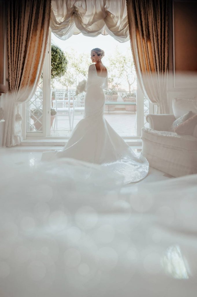 Bride standing in a luxurious room with soft light and terrace views in Amalfi