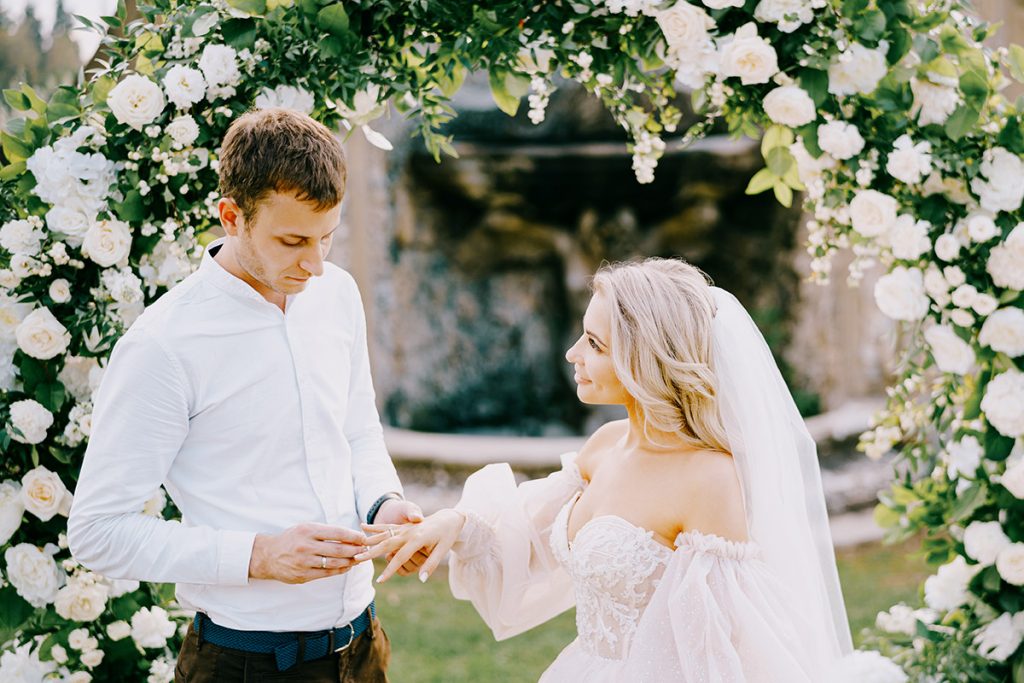 Bride and groom exchanging rings under a flower arch, captured by a Puglia wedding photographer