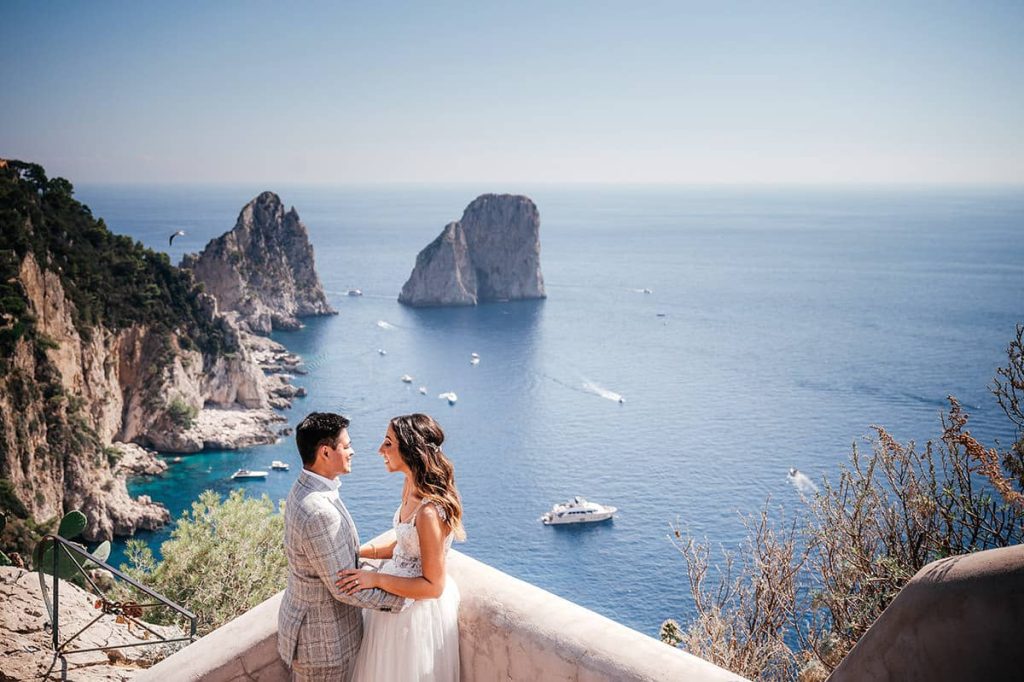 Italian Wedding Photographer captures a couple with a stunning view of the Faraglioni rocks in Capri, showcasing the island's beauty
