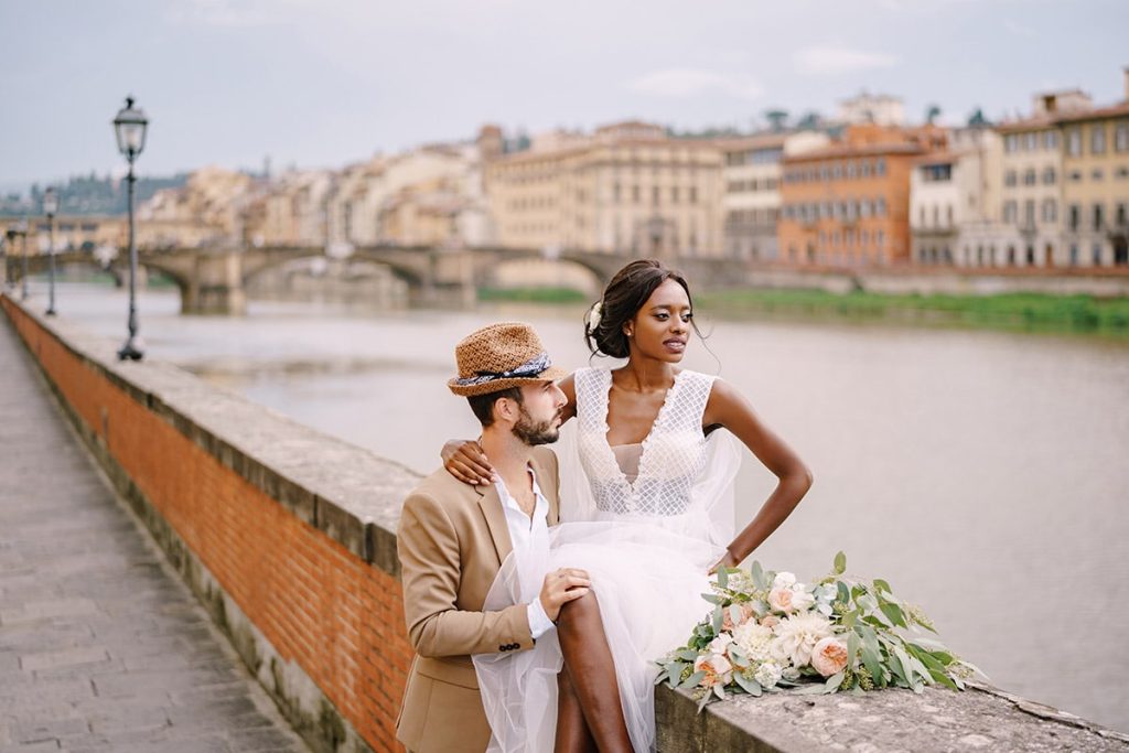 Italian Wedding Photographer captures a stylish couple with the Ponte Vecchio in Florence as a backdrop, showcasing the city's cultural charm