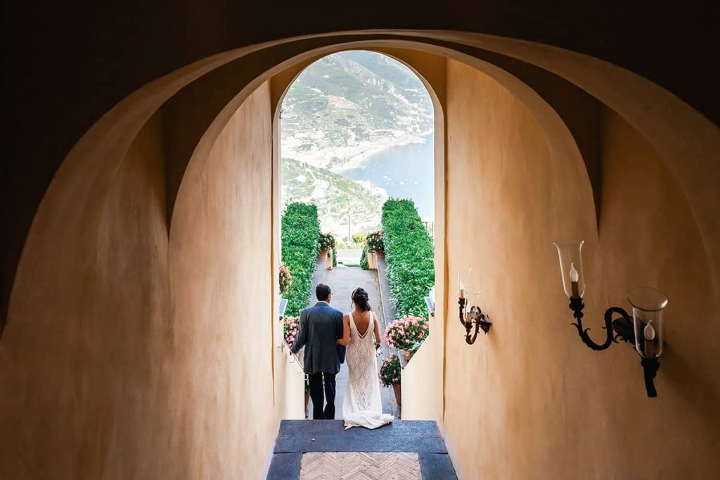 Bride and groom walking through an arched doorway at Belmond Hotel Caruso wedding Ravello, with a view of the garden
