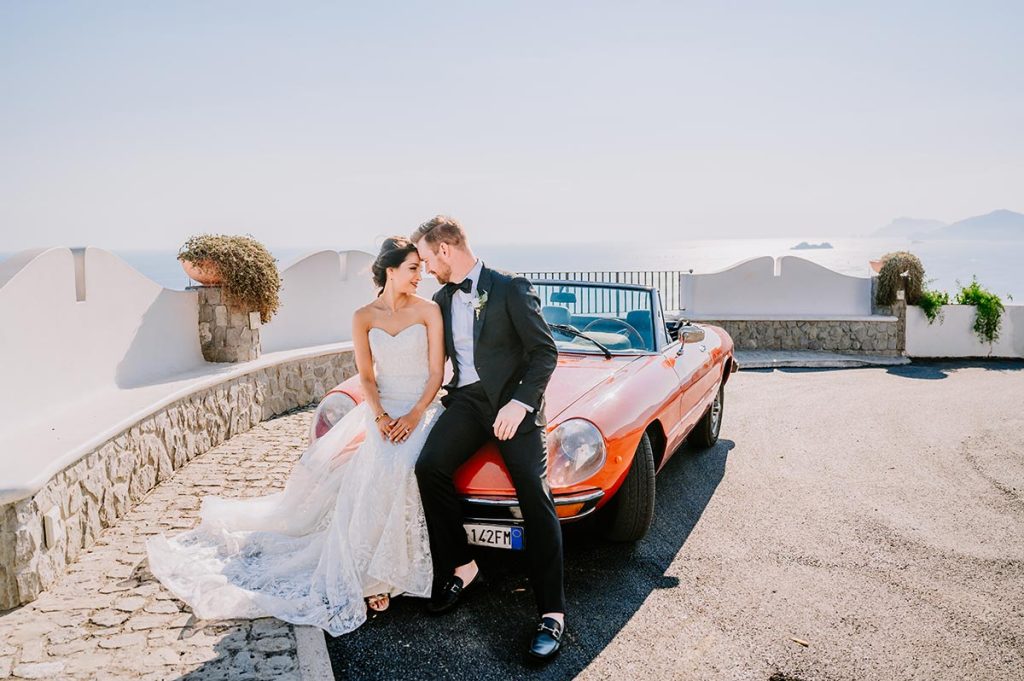 Amalfi Coast Wedding Planner image of a bride and groom by a vintage car, emphasizing the stylish and unique transportation option