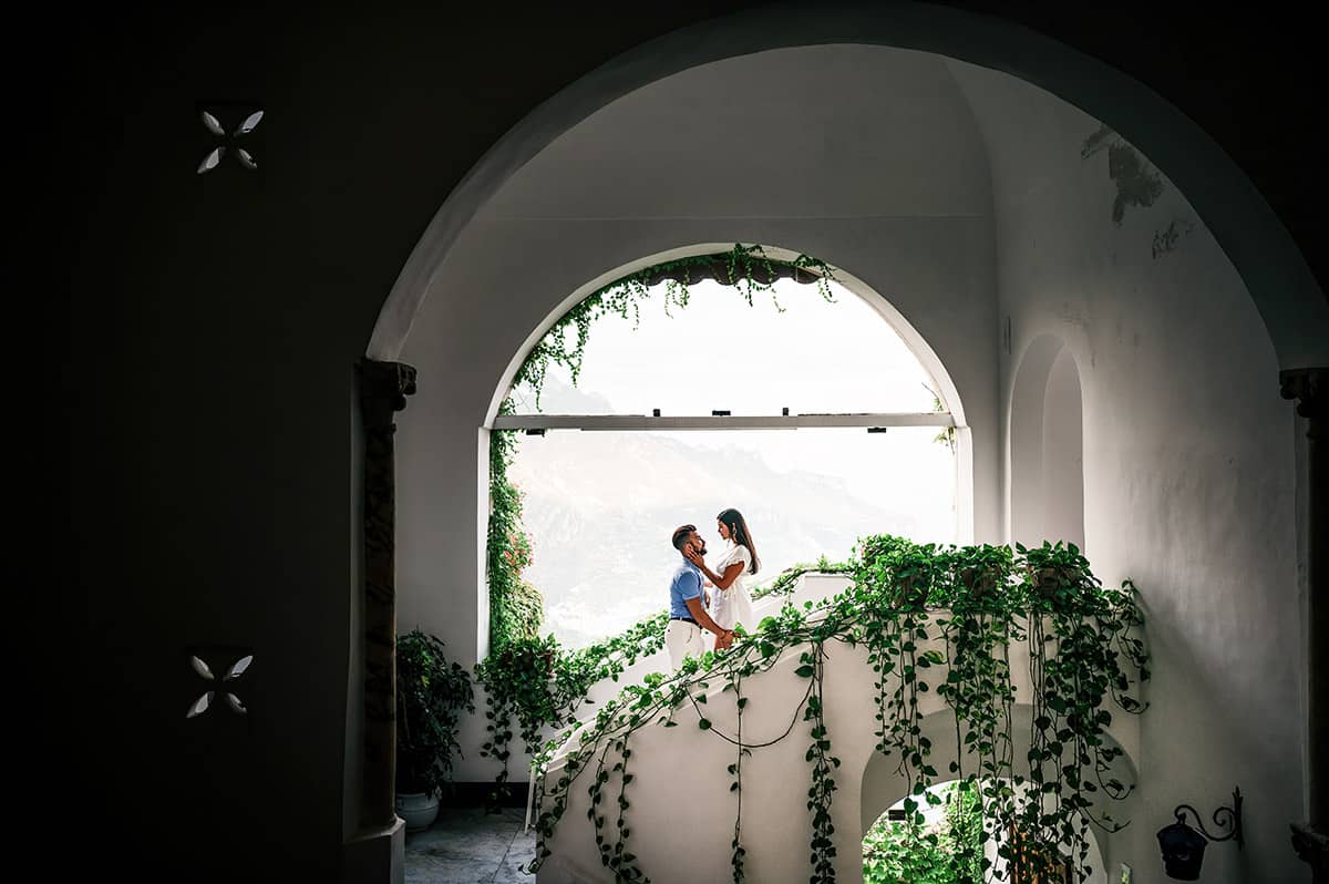 Couple on Ivy Staircase, Italy Couple in light blue and white on a white staircase adorned with ivy, overlooking a scenic Italian landscape