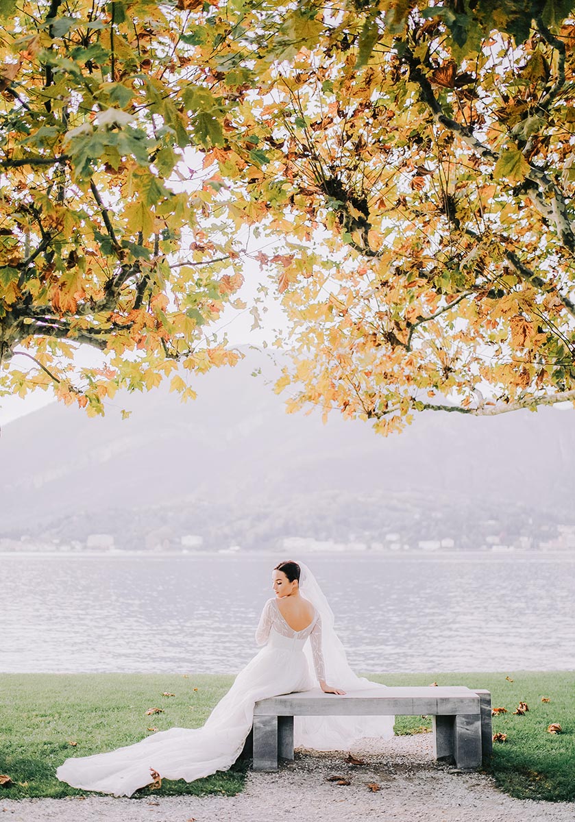 Bride with a flowing train sits on a bench by Lake Como, a serene moment captured by a Lake Como wedding photographer