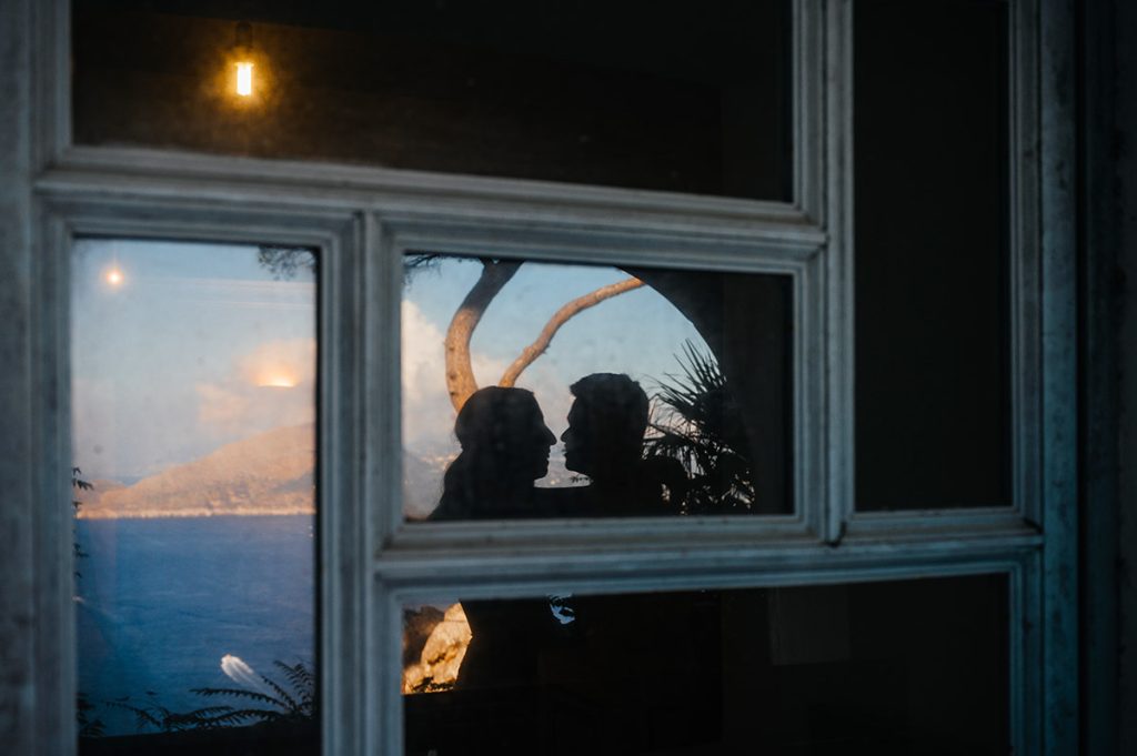 Couple's silhouette framed in a window reflecting a Capri sunset, capturing a romantic moment of a wedding in Capri