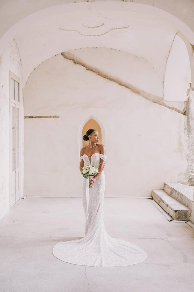 A Capri wedding photographer captures a bride in an elegant white gown standing in a historic, arched hallway