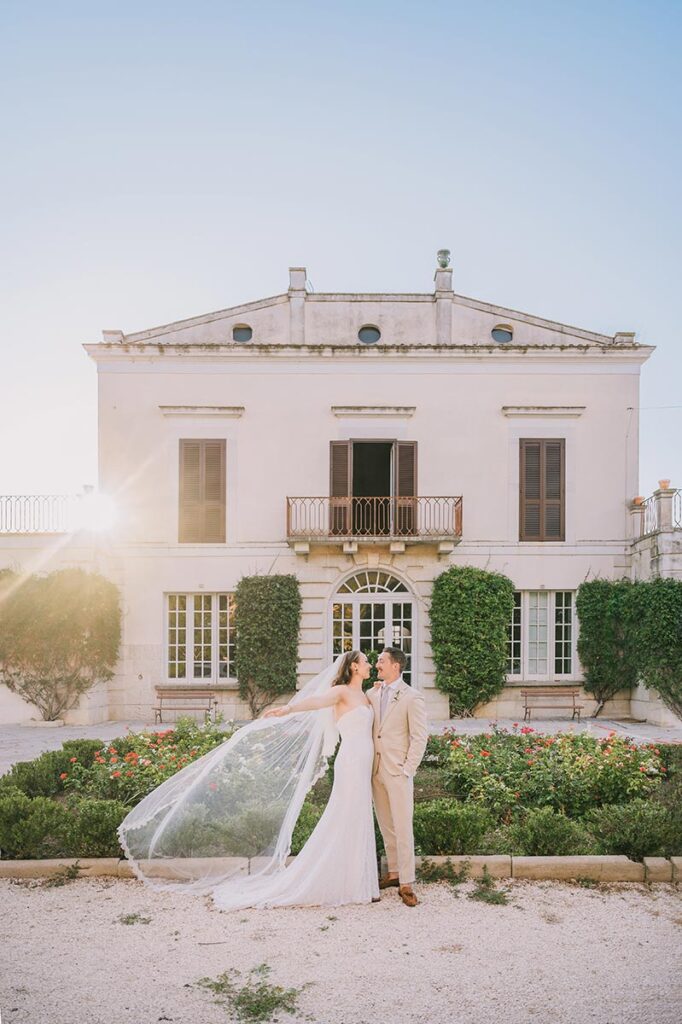 Wedding couple posing in front of a sunlit Apulian villa, captured by a Puglia wedding photographer
