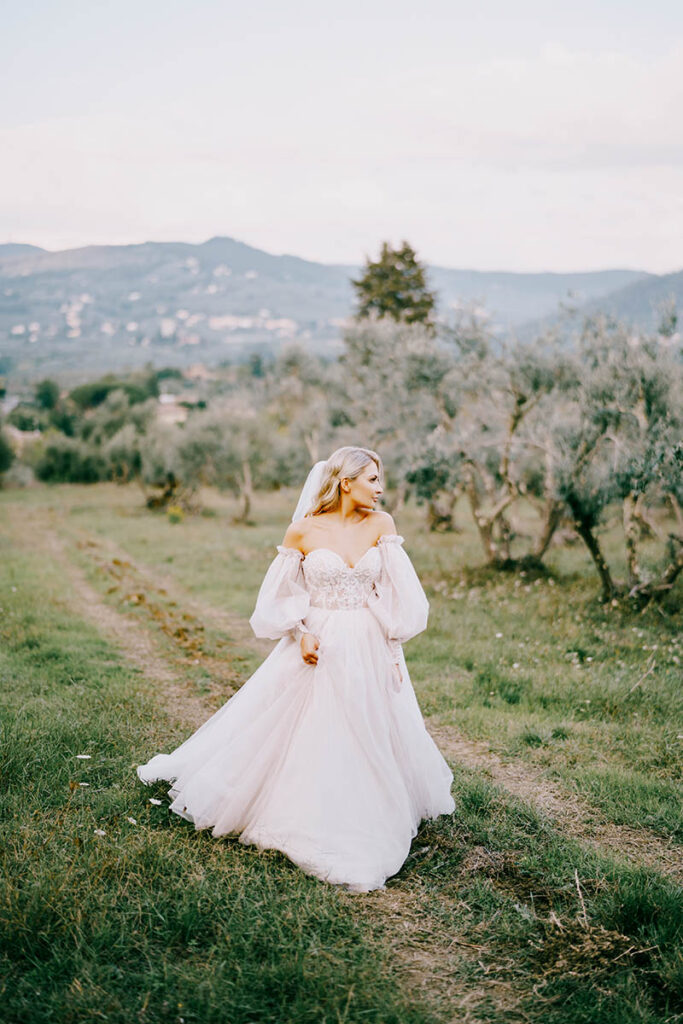 Bride in white dress walks a path, part of an Arezzo wedding planner's event