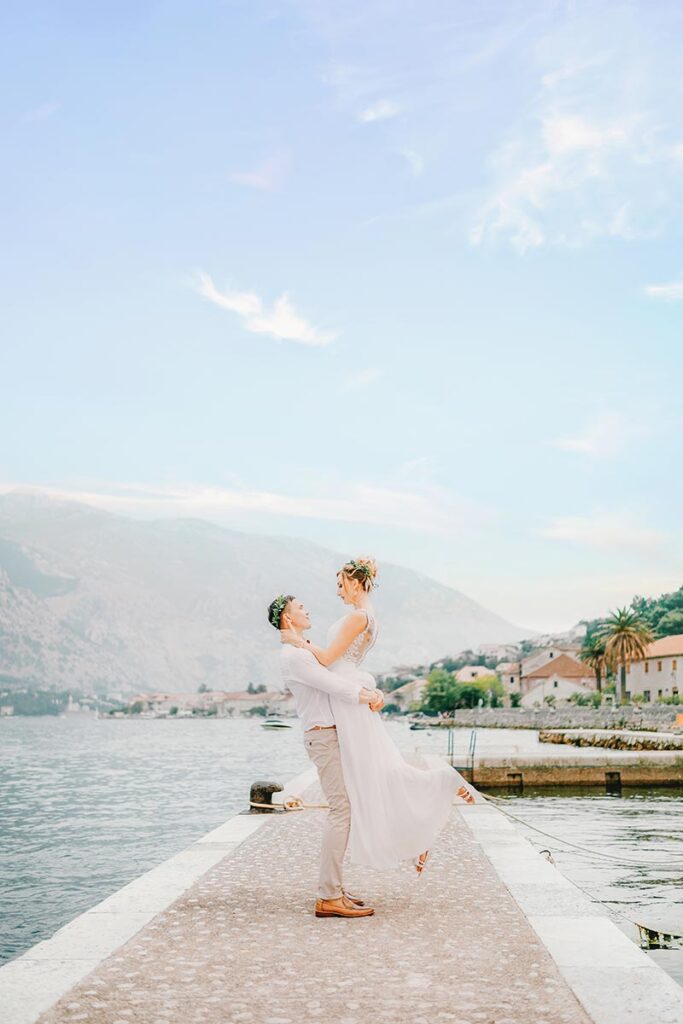 Bride and groom on a pier with a lakeside town in the distance, a shot by a Lake Como wedding photographer