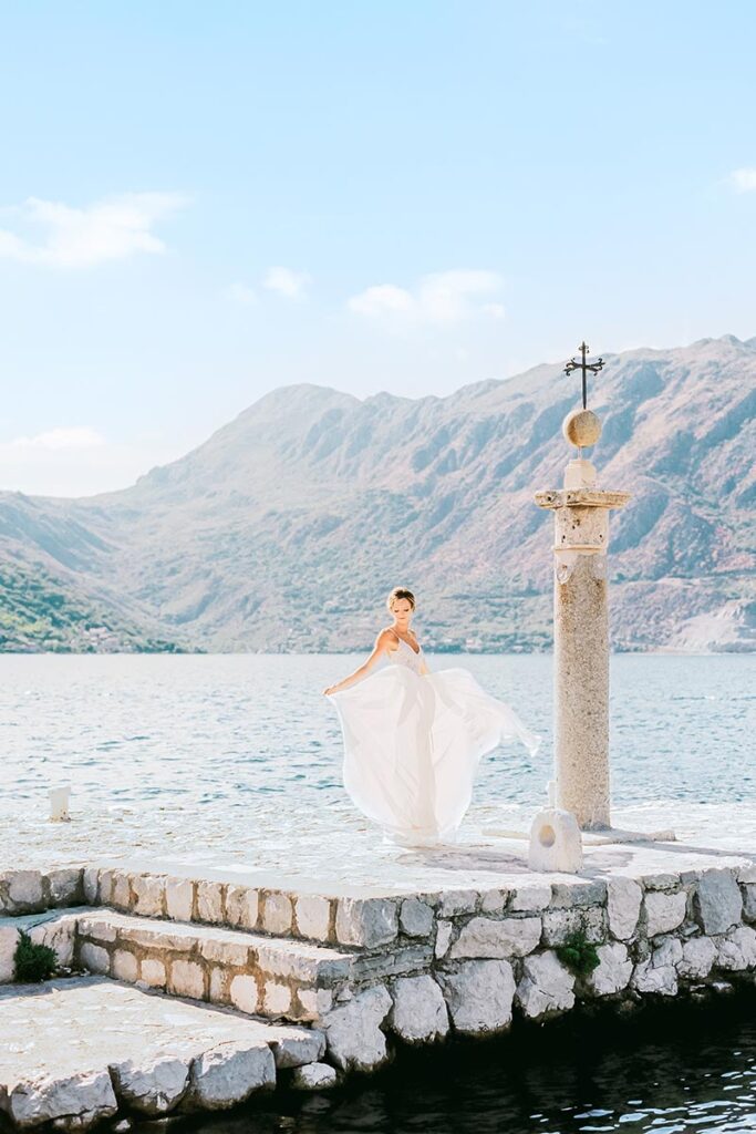 Bride in a white gown on a stone platform with Lake Como and mountains, captured by a Lake Como wedding photographer