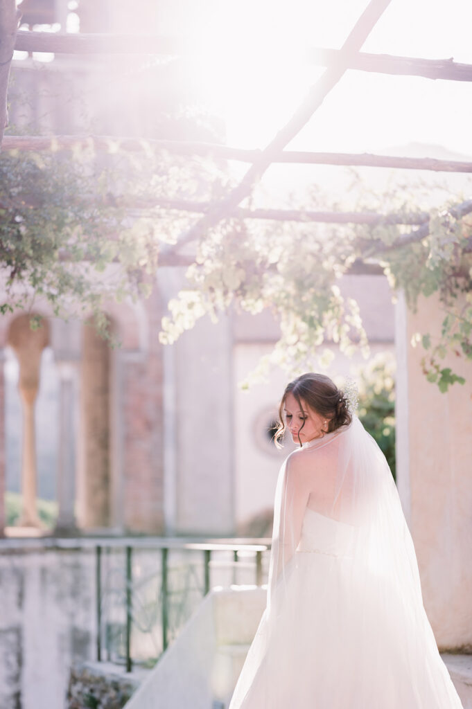 Bride under a pergola with soft sunlight filtering through vines, in Amalfi Coast villa