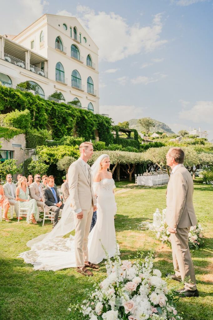 Bride and groom exchanging vows on a lawn at their Belmond Hotel Caruso wedding Ravello, with guests seated