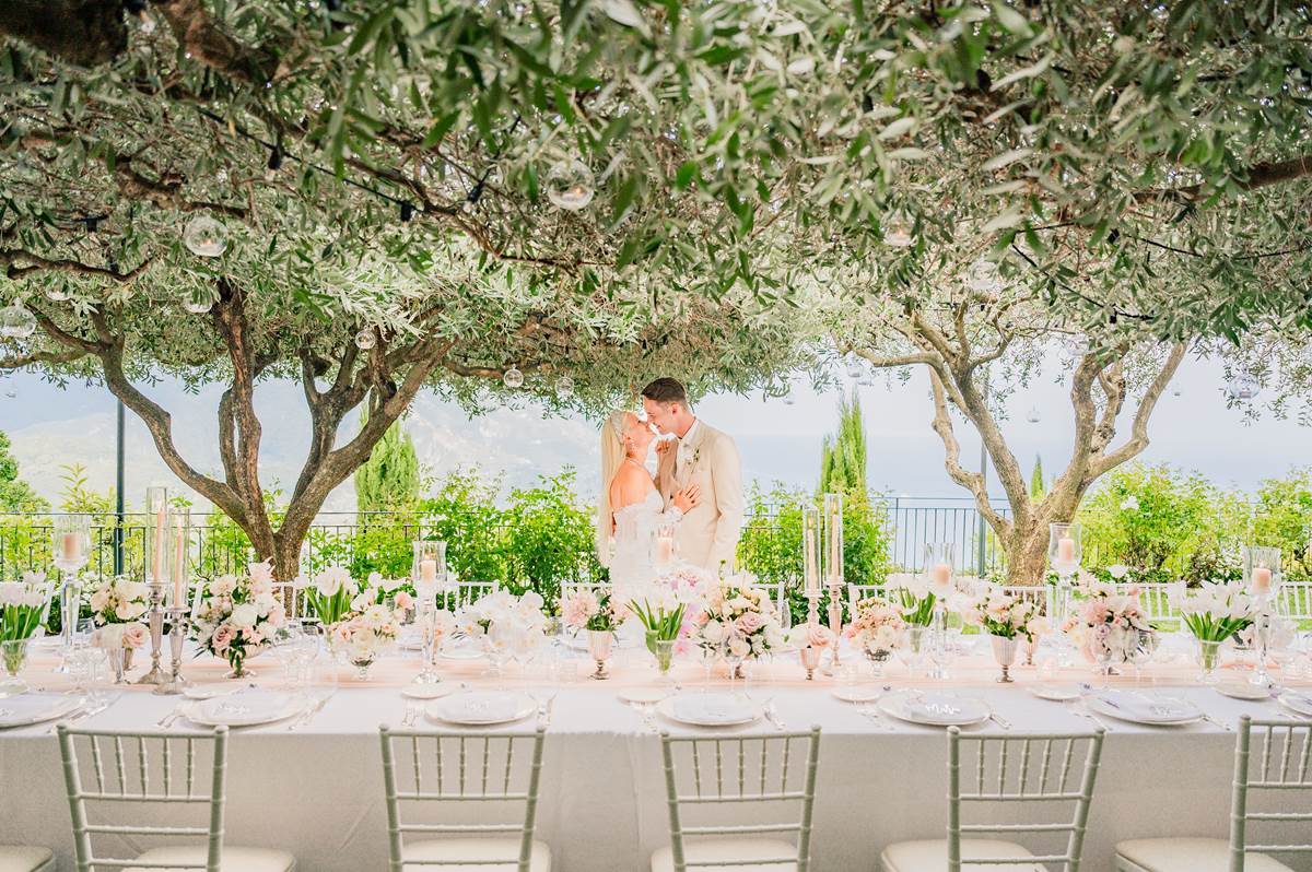 Amalfi Coast Wedding Planner showcasing a beautifully set outdoor reception with a kissing couple under olive trees, highlighting the romantic setting